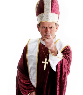 A man dressed as a religious official with a cross necklace pointing his finger in disapproval.