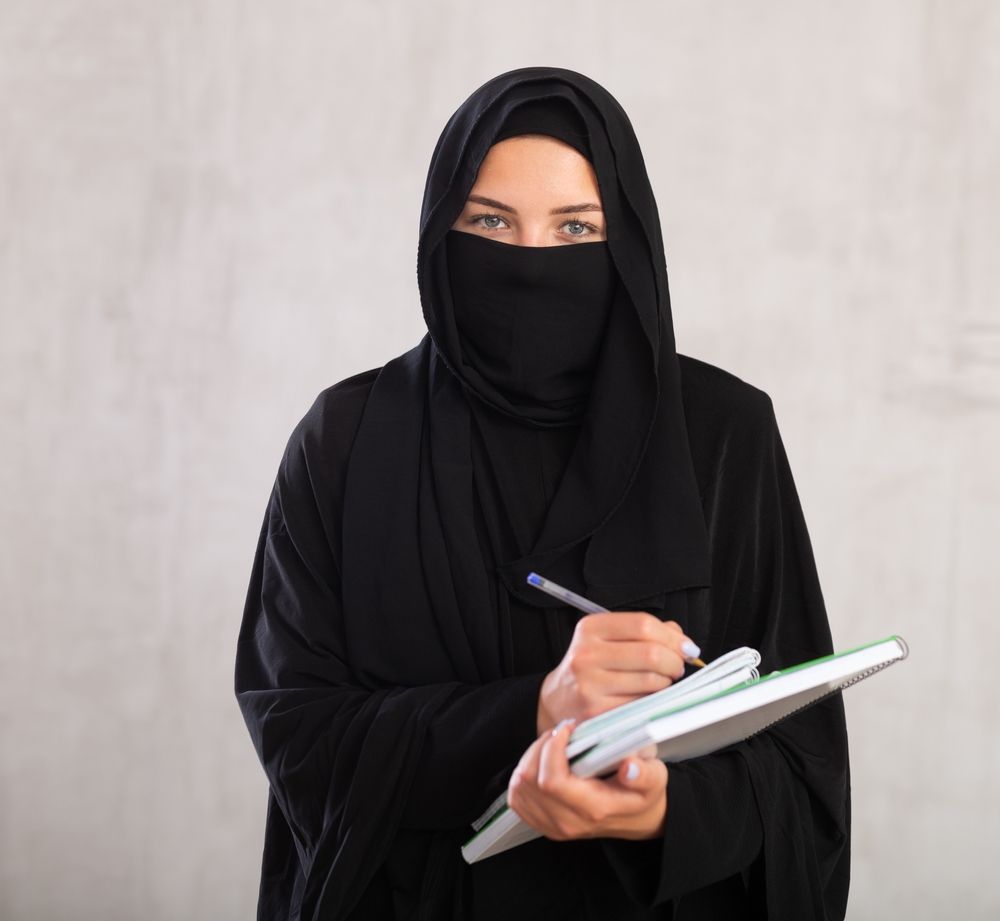 A Muslim professional wearing a niqab and holding notebooks