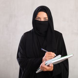 A Muslim professional wearing a niqab and holding notebooks